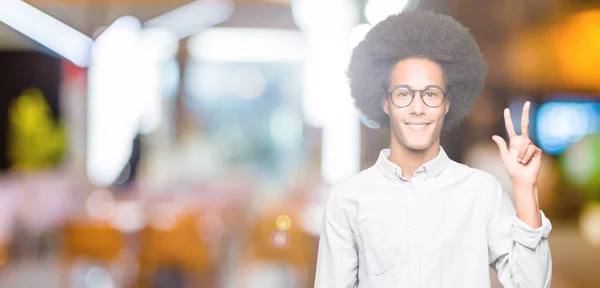 眼鏡を指で上向きの表示とアフロの髪の若いアフリカ系アメリカ人は自信を持って 幸せな笑みを浮かべている間ナンバースリーします — ストック写真