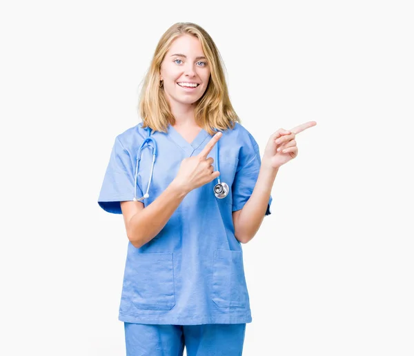 美丽的年轻医生妇女穿着医疗制服在孤立的背景微笑 看着相机指向用两只手和手指的一侧 — 图库照片