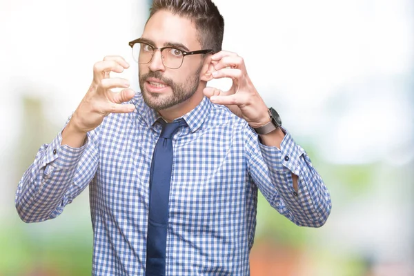 Young business man wearing glasses over isolated background Shouting frustrated with rage, hands trying to strangle, yelling mad