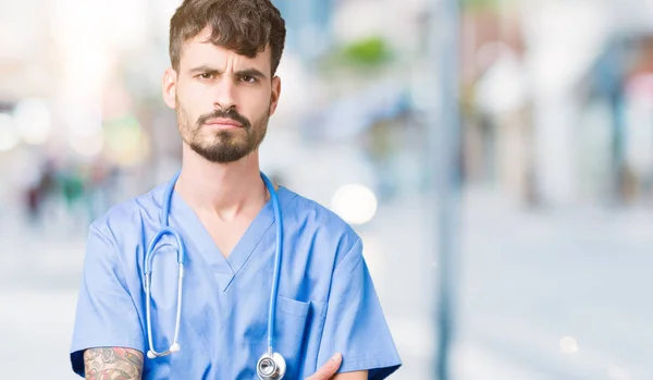 Young handsome nurse man wearing surgeon uniform over isolated background skeptic and nervous, disapproving expression on face with crossed arms. Negative person.