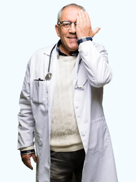 英俊的资深医生穿着医疗外套 用手捂住一只眼睛 脸上带着自信的微笑和惊喜的情绪 — 图库照片
