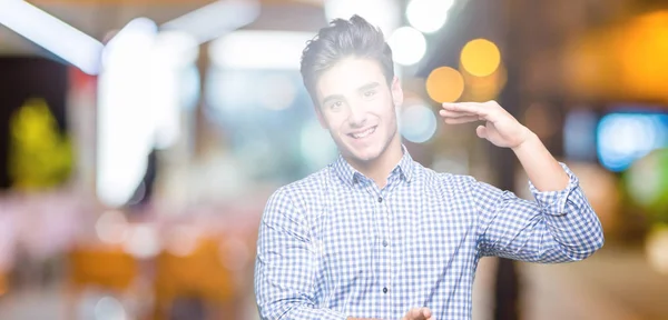 Young handsome business man over isolated background gesturing with hands showing big and large size sign, measure symbol. Smiling looking at the camera. Measuring concept.