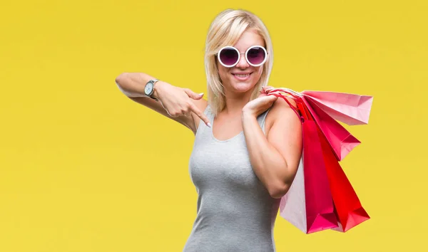 自分自身に驚き顔ポインティング指で孤立した背景の上販売開催ショッピング バッグをショッピング若い美しいブロンドの女性 — ストック写真