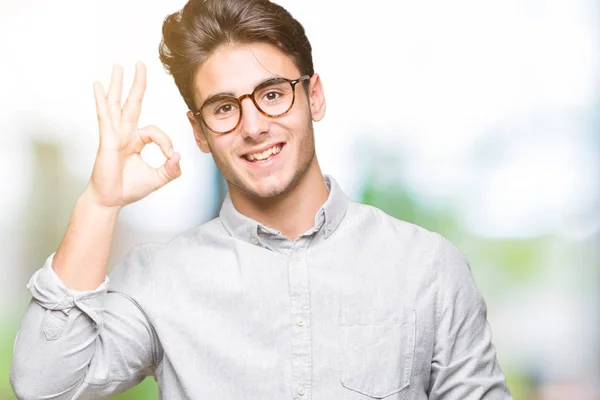 孤立した背景を浮かべて手と指で サインをしている肯定的な上メガネの若いハンサムな男 成功した式 — ストック写真