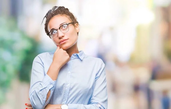 Young braided hair african american business girl wearing glasses over isolated background with hand on chin thinking about question, pensive expression. Smiling with thoughtful face. Doubt concept.