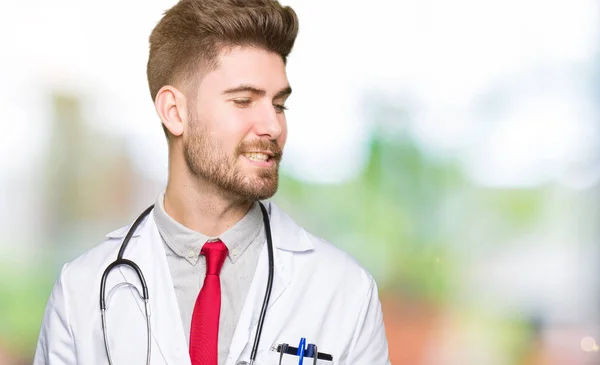 若いハンサムな医者 自然な表現の顔に笑みを浮かべて側に離れて見て着て医療コートの男 自信を持って笑ってください — ストック写真