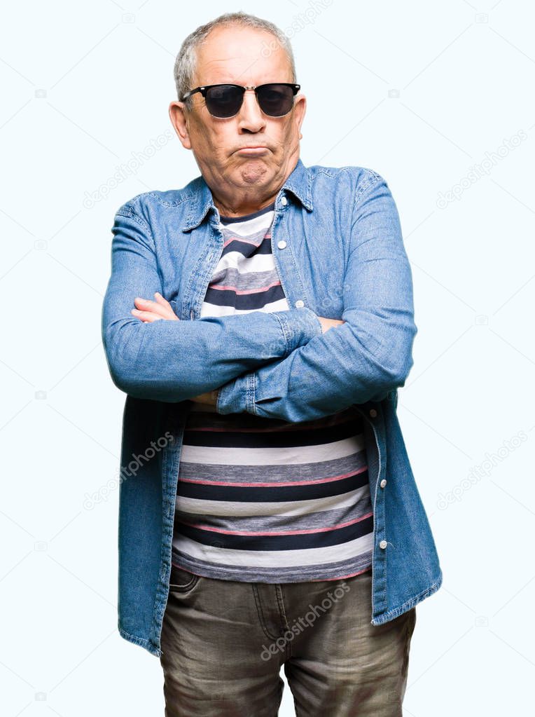 Handsome senior man wearing denim jacket and sunglasses skeptic and nervous, disapproving expression on face with crossed arms. Negative person.