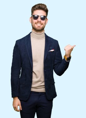 Genç yakışıklı zarif adam arıyor ve başparmak yanında yukarıyı mutlu yüz ile gülümseyen güneş gözlüğü takıyor.