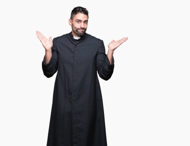 Genç Hıristiyan rahip üzerinde izole arka plan clueless ve şaşkın bir ifadeyle kollar ve eller kaldırdı. Şüphe kavramı.