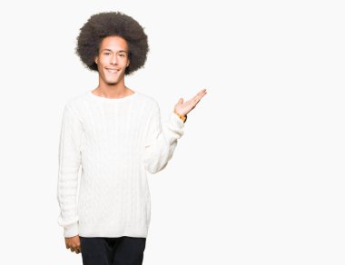 Neşeli sunulması ve kameraya bakarak avucunun ile işaret gülümseyen kış kazak giyen afro saçlı genç Afro-Amerikan adam.