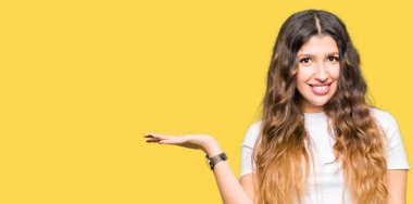 Neşeli sunulması ve kameraya bakarak avucunun ile işaret gülümseyen casual beyaz t-shirt giyen genç güzel kadın.