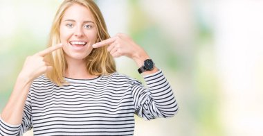 Kendinden emin gösterilen ve işaret parmakları diş ve ağız ile gülümseyen izole arka plan üzerinde çizgili süveter giyen güzel genç kadın. Sağlık kavramı.