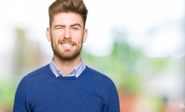 Genç yakışıklı bussines adam seksi bir ifadeyle, neşeli ve mutlu yüzünü kameraya bakarak göz kırpıyor.