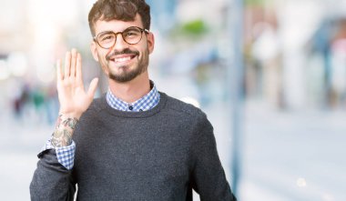 Genç yakışıklı zeki adam izole arka plan Waiving mutlu selam söyleyerek üzerinde gözlük ve gülümseyen, dostça karşılama jest