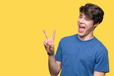 Mutlu yüz zafer işareti yaparken kameraya göz kırpıyor ile gülümseyen izole arka plan üzerinde mavi t-shirt giyen genç yakışıklı adam. İki numaralı.