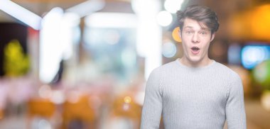 Korkuyor ve şok sürpriz ifade, korku ve heyecan yüz ile izole arka plan üzerinde kış kazak giyen genç yakışıklı adam.