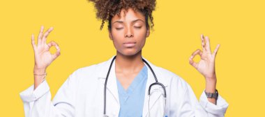 Genç Afro-Amerikan doktor kadın izole arka plan üzerinde dinlenmek ve gülümseyen gözlerle parmak ile meditasyon jest yapıyor kapalı. Yoga kavramı.