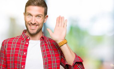 Yakışıklı adam rahat gömlek Waiving selam söyleyerek mutlu ve gülümseyerek giyiyor, dostça karşılama jest