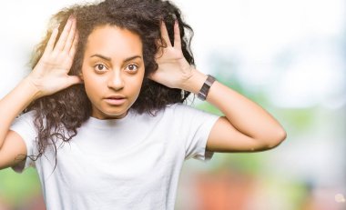 Rahat beyaz t-shirt giyen kıvırcık saçlı Genç güzel kız iki elini de kulak jestinde duymaya çalışıyor, dedikoduyu merak ediyor. İşitme sorunu, sağır