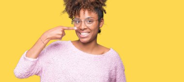 Güzel genç Afro-Amerikan kadın gözlük izole üzerinde işaretleme için yüz ve burun, neşeli gülümseyerek el parmak ile arka plan