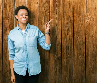 Yüzünde büyük bir gülümseme ile izole arka plan üzerinde genç güzel Afrikalı Amerikalı kadın, kamera bakarak yan el ve parmak ile işaret.