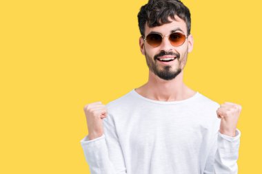 Yakışıklı delikanlı izole arka plan kutlama üzerinde güneş gözlüğü takıyor şaşırttı ve başarı için kaldırdı kollarını açarak hayret ve gözleri açık. Kazanan kavramı.