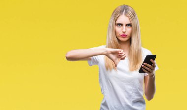 Kızgın yüz, eksi işareti aşağı antipati başparmak ile gösterilen, ret kavramı ile izole arka plan üzerinde akıllı telefon kullanan genç güzel sarışın kadın