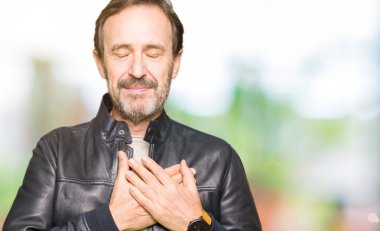 Orta yaş yakışıklı adam siyah deri ceket ile gülümseyen giyen kapalı gözler ve yüzünde minnettar jest ile göğüs üzerinde eller. Sağlık kavramı.