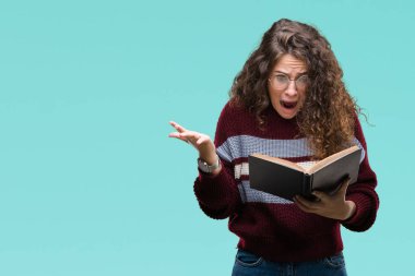 Genç esmer kız kocaman bir gülümseme ile çığlık zaferini kutluyor ve ellerini kaldırdı izole arka plan çok mutlu ve heyecanlı, kazanan ifade üzerinde gözlük takan bir kitap okuma