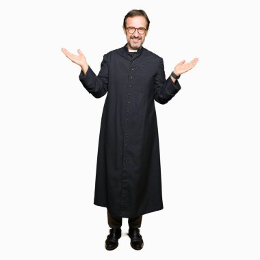 Katolik giyen orta yaş rahip adam robe iki elin avuç içi açık gösterilen, sunmak ve reklam karşılaştırma ve denge gülümseyen