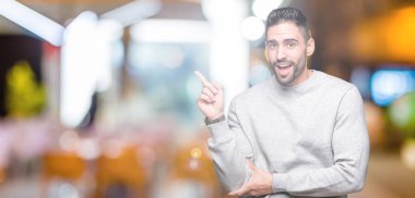 Kameraya bakarak yan el ve parmak ile işaret yüzünde kocaman bir gülümseme ile izole arka plan üzerinde sweatshirt giyen genç yakışıklı adam.