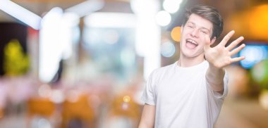 Yakışıklı delikanlı gösterilen ve parmakları ile işaret izole arka plan üzerinde rahat beyaz t-shirt giyen beş kendinden emin ve mutlu gülümseyerek iken numara.