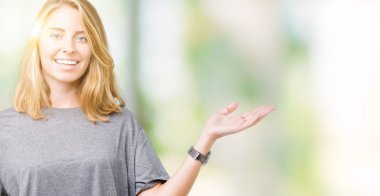 Neşeli sunulması ve kameraya bakarak avucunun ile işaret gülümseyen izole arka plan üzerinde büyük boy rahat t-shirt giyen güzel genç kadın.