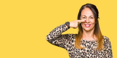 Leopar hayvan baskı elbise giyen güzel orta yaş kadın yüz ve burun, neşeli gülümseyen el parmak ile Işaret