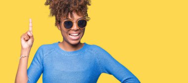 Güzel genç Afro-Amerikan kadın başarılı fikirle izole arka plan işaret parmağı üzerinde güneş gözlüğü takıyor. Çıktıktan ve mutlu. Bir numara.