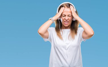 Orta yaş İspanyol kadın kulaklık çünkü umutsuz ve stresli baş ağrısı acı izole arka plan üzerinde giyen müzik dinlemek ağrısı ve migren. Ellerini kafasına.