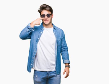 Genç yakışıklı adam giyen güneş gözlüğü izole üzerinde işaretleme için yüz ve burun, neşeli gülümseyerek el parmak ile arka plan