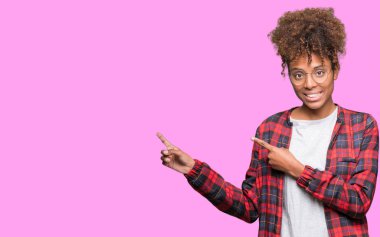 Güzel genç Afro-Amerikan kadın gülümseyerek ve iki elleri ve parmakları ile tarafına işaret kamera bakarak izole arka plan üzerinde gözlük.