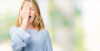 Güzel genç kadın yarım yüz, göz ve ağız el ile kapsayan yorgun esneme izole arka plan üzerinde mavi kazak giyiyor. Acı yüzü acıyor.