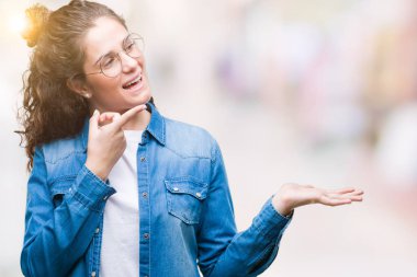 Hayret ve el ile sunulması ve parmak ile işaret ederken kameraya gülümseyen izole arka plan üzerinde gözlük güzel genç esmer kıvırcık saçlı kız.