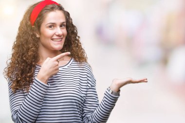 Üzerinden hayran ve el ile sunulması ve parmak ile işaret ederken kameraya gülümseyen izole arka plan çizgili süveter giyen güzel esmer kıvırcık saçlı Genç kız.