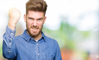 Genç yakışıklı sarışın adam giyiyor rahat kot gömlek öfkeli ve sinirli sinirli ve öfke ile bağırarak süre öfkeli yumruk yükselterek. Öfke ve agresif kavramı.