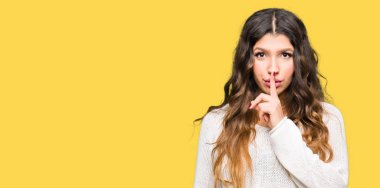 Dudaklarında parmak ile sessiz olmanı beyaz kazak giyen genç güzel kadın. Sessizlik ve gizli kavramı.