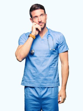 Çene düşünme hakkında soru, dalgın ifade üzerine el ile izole arka plan üzerinde tıbbi üniforma giyen yakışıklı Doktor adam. Düşünceli yüzüyle gülümsüyor. Şüphe kavramı.