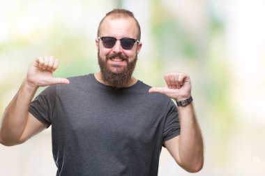 Yüzünde gülümseme ile kendinden emin görünüyorsun, kendini gururlu ve mutlu parmakları ile işaret izole arka plan üzerinde güneş gözlüğü takmış Genç beyaz hipster adam.