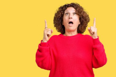 Güzel orta ager üst düzey kadın kırmızı kış kazak üzerinden hayran ve yukarıya bakıyor ve parmakları ile işaret ve silah kaldırdı sürpriz arka plan izole.