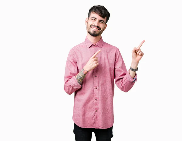 年轻英俊的男人穿着粉红色的衬衫在孤立的背景微笑着 看着相机指向镜头 用两只手和手指指着一边 — 图库照片
