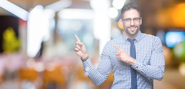 Young business man wearing glasses over isolated background smiling and looking at the camera pointing with two hands and fingers to the side.