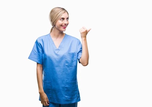 探していると親指のアップが付いている側面を指している幸せそうな顔を浮かべて隔離された背景に看護師女性の若い美しい金髪の医者の外科医 — ストック写真