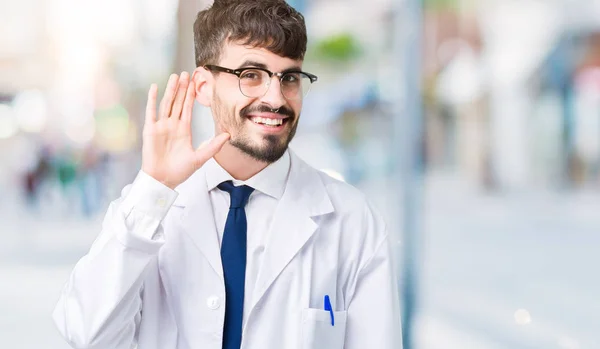 若いプロの科学者男は 噂やゴシップに審理をリスニングの耳に手を浮かべて分離の背景に白のコートを着てします 難聴の概念 — ストック写真